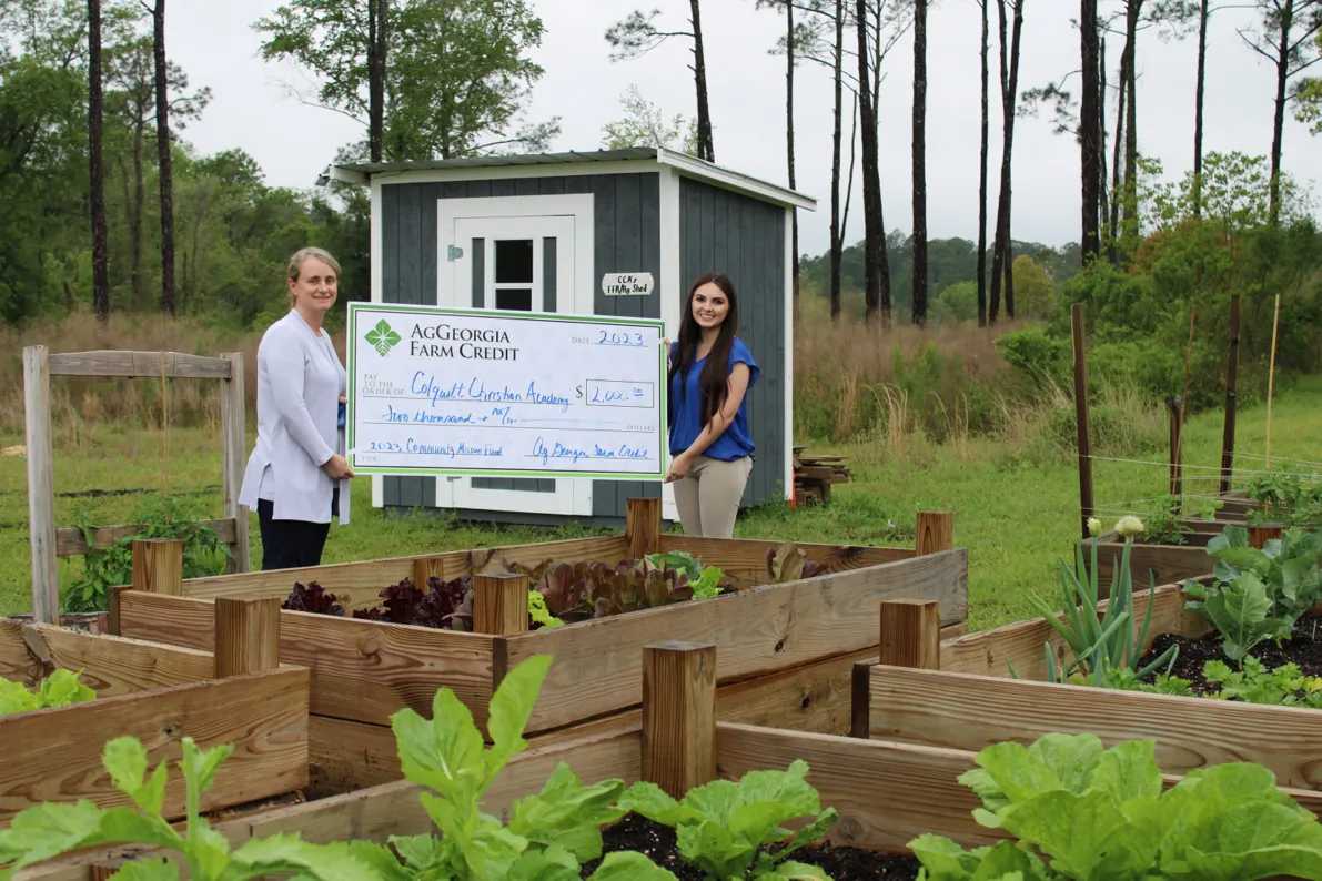 Two people holding a large check in a garden.