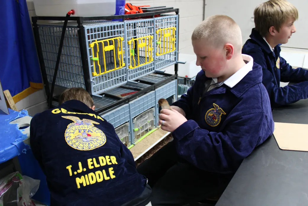 Children with "T.J. Elder Middle" jackets on holding small animals.